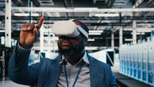 Server farm employee puts on a VR headset for network management while using virtual reality simulation to oversee data center infrastructure rigs.