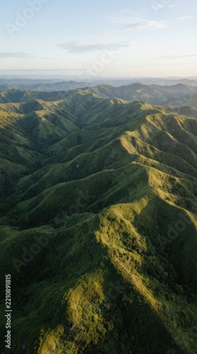 Aerial view of rolling green hills landscape at sunrise, showcasing natural mountain ridges and lush valley terrain in soft morning light