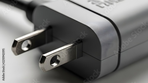 Close up shot of a gray electrical plug with two metallic prongs on a plain background, symbolizing power and connectivity