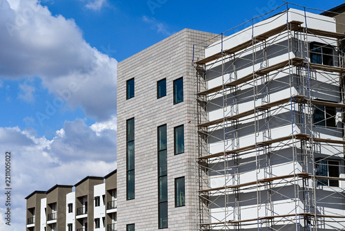 Apartment complex under construction with buildings at various stages of completion, including scaffolding and finished facades, illustrating multifamily housing development and urban growth