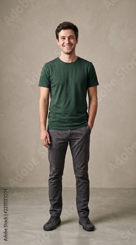 Full length portrait of a smiling young man standing against a neutral studio background wearing a green tshirt and grey trousers