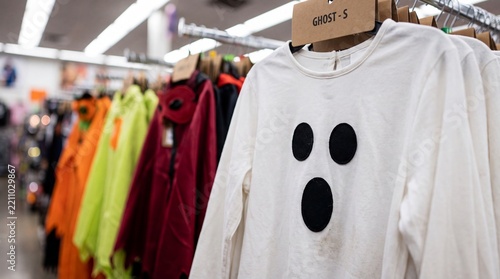 A white ghost costume shirt hanging on a clothing rack inside a retail store aisle with other colorful costumes white long sleeved design hangs metal