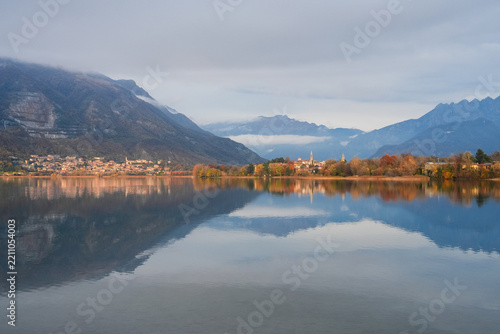 Pusiano lake, located between provinces of Como and Lecco, in Brianza, Italy. Mountain lake with calm water reflecting village, autumn trees, scenic view of Italian countryside surrounded by alps