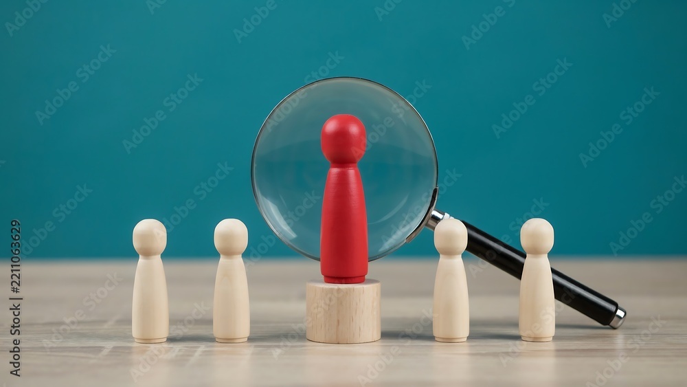 Obraz premium Red Wooden Figure Under Magnifying Glass Standing Out from a Group, Concept of Talent Identification, Candidate Selection and Recruitment