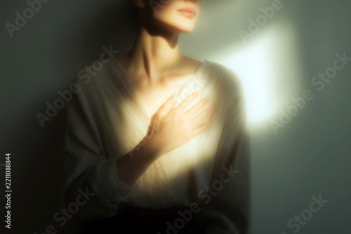 Intimate soft portrait of a person with hand over heart in warm window light for emotional background and wellness poster design