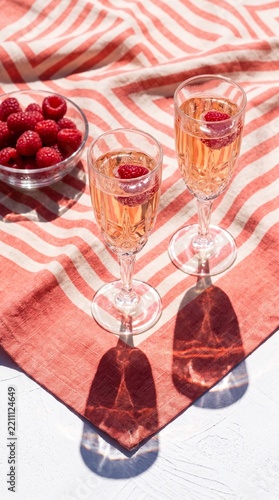 Two glasses of sparkling rosé with raspberries in sunlight