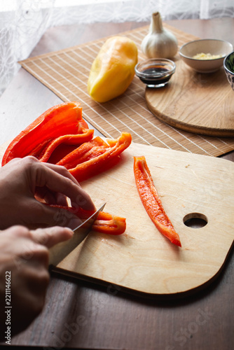 Hand cutting red bell pepper on a wooden cutting board