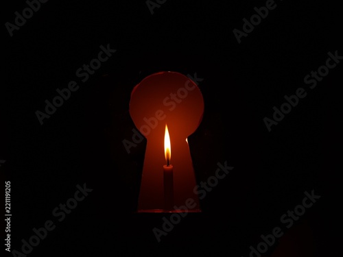 Fotografie A candle light glowing brightly in the dark, viewed through the silhouette of an old keyhole