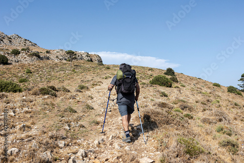 Obraz na plátně Hiker ascending mountain trail with backpack and trekking poles