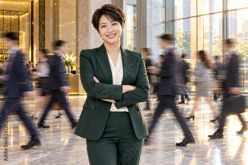 Naklejka 분주한 유리 로비에서 팔짱을 끼고 미소 짓는 한국인 중년 여성 리더