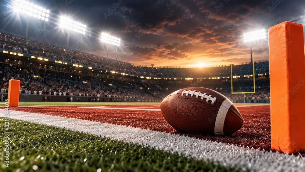 Obraz premium American football beside an orange pylon in a stadium end zone at sunset