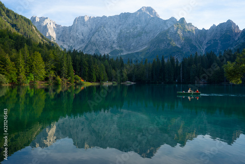 Scenic mountain lake with reflection and rowboat carrying two people in a peaceful forest setting