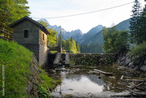 small hydroelectric power station on river with forest and rocky mountain landscape in the background