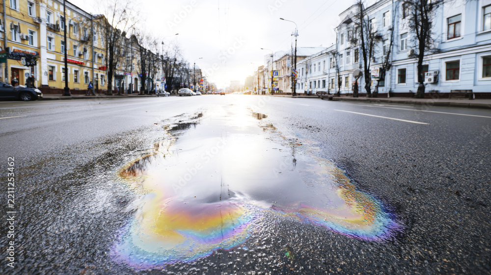 Obraz premium Oil spill creating colorful iridescent rainbow puddle on urban asphalt road, showing environmental pollution