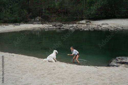Young girl playfully pulling her reluctant dog into a lake