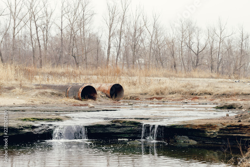 Rusty industrial pipes draining into a polluted stream