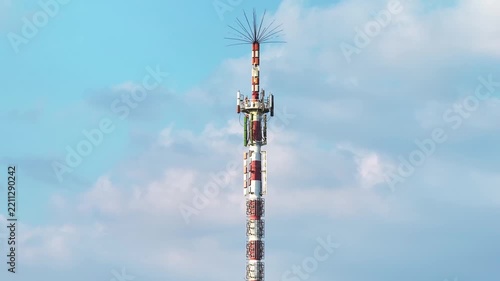 Red and White Telecommunication Antenna Tower Against Blue Sky with Clouds