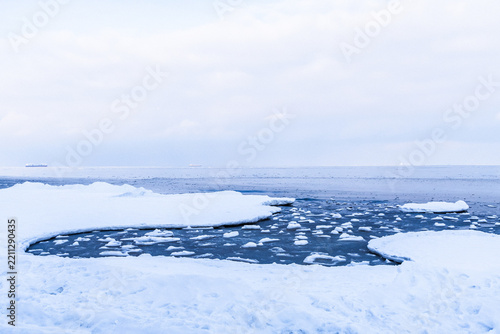 Frozen landscape with ice patches and open water under cloudy sky