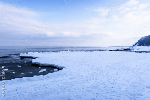 Frozen shoreline with ice and snow under a cloudy blue sky