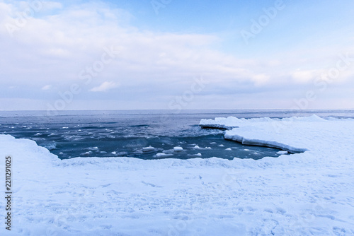 Frozen shoreline with ice formations and calm water under cloudy sky