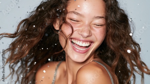 Young woman with curly hair laughing joyfully under falling confetti