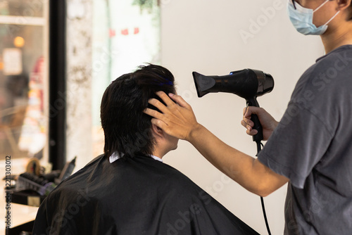Professional hairstylist using electric hair clippers to trim and shape a client in hair salon.