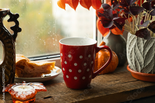 Cozy fall vibes. Red polka dotted mug of tea or coffee on windowsill on rainy autumn day. 