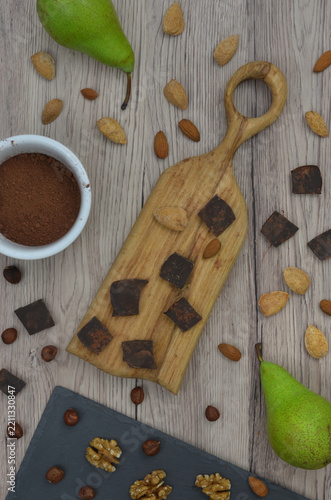 Chocolate and green pears, nuts and almonds, cocoa powder in a bowl on wooden background. Ingredients for an autumn or winter chocolate dessert, cupcakes or hot, cocoa drink.