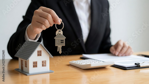 Professional holding house keys and a miniature home model on a desk