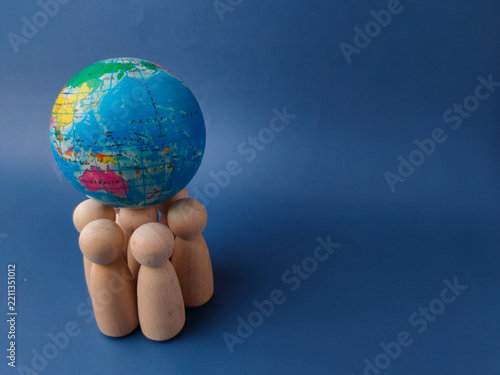 A cluster of wooden peg figures stands together while supporting a small globe on a blue background