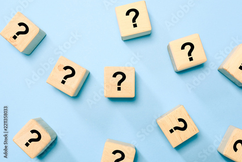 Wooden blocks with question marks scattered on a blue background, representing questions, uncertainty, problem solving, curiosity, decision making, confusion, research, and finding answers.