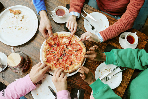 Diverse young adult friends sharing pizza around cafe table. Concept ideal for restaurant marketing, social media promotion and food delivery campaigns, top view