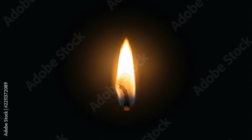 A single bright candle flame burning with a warm orange glow against a dark black background in a quiet room
