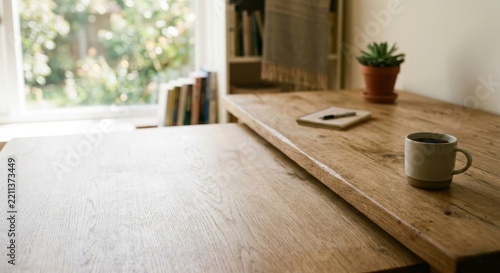 Rustic wooden desk workspace in a bright home office featuring a ceramic coffee mug, open notebook with pen, and small succulent plant near a window with blurred bookshelf background