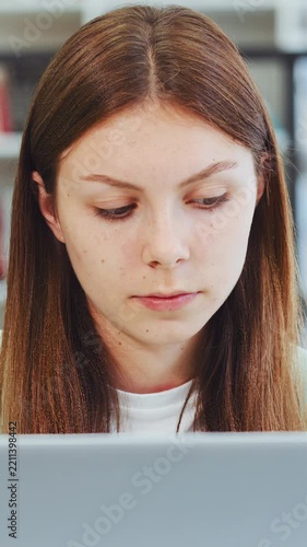 Serious girl student looking at laptop screen while doing research in university library. Concentrated woman working on computer projects