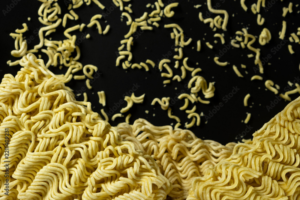 Obraz premium Instant noodle brick next to scattered dry crumbs on black backdrop