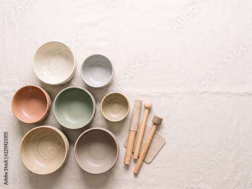 Collection of earth-tone ceramic bowls and wooden mallets on wrinkled linen