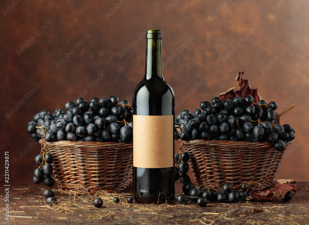 Obraz premium Bottle of red wine and blue grapes in old basket.