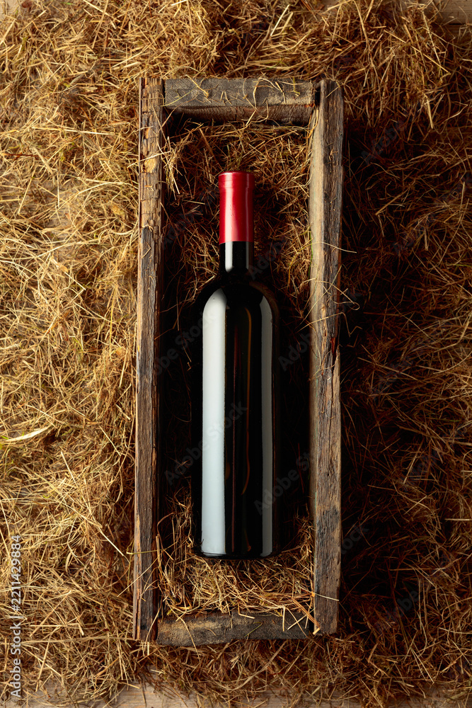 Obraz premium Bottle of red wine in an antique wooden box on a table covered with hay.