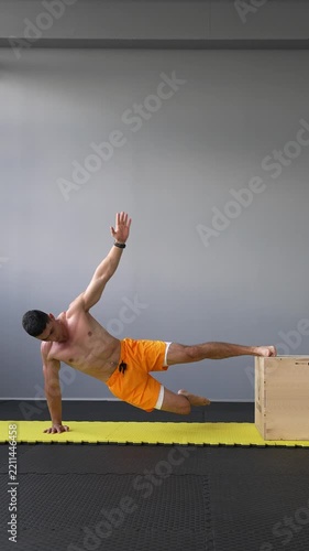 Muscular man performs an elevated side plank with feet supported on a plyo box. Core strength, balance, stability and bodyweight fitness concepts. Vertical video.