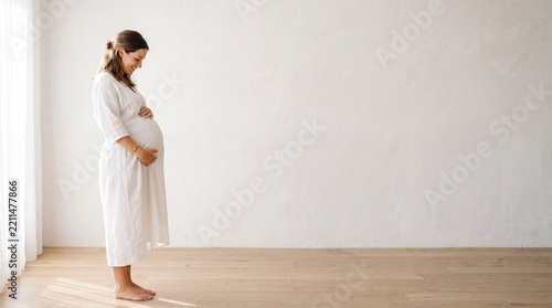 Smiling Pregnant Woman in White Dress in Minimalist Room
