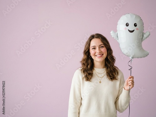 Happy young woman holding a cute ghost balloon on purple background