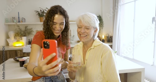 Young woman and her senior grandmother using a cellphone for a video call while drinking wine