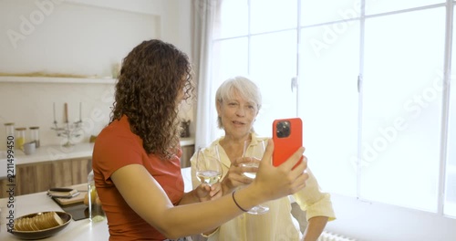 Cheerful grandmother and granddaughter enjoying a video conference on a smartphone in the kitchen