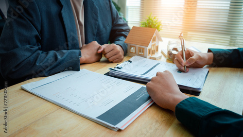Fotografie Real estate agen reviewing and signing property documents beside a model house and savings jar, illustrating real estate contracts, mortgage planning, home purchase, and property investment