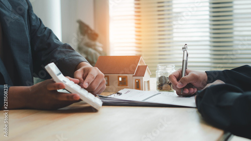 Real estate agen reviewing and signing property documents beside a model house and savings jar, illustrating real estate contracts, mortgage planning, home purchase,  and property investment.