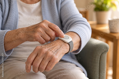 Older adult pressing a wearable emergency alert button at home. Senior independent living and personal safety. Medical alert device for aging in place. Home care and fall prevention.