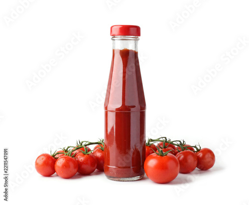 Glass bottle of homemade ketchup tomato sauce surrounded by fresh ripe tomatoes on white background