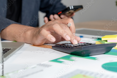 A close up shot of a man using a calculator to manage his monthly financial expenses and personal budget at a desk.
