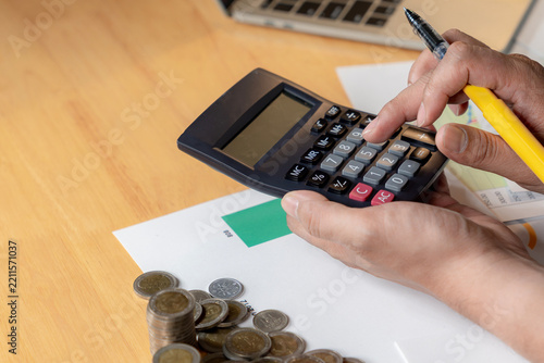 A close up shot of a man using a calculator to manage his monthly financial expenses and personal budget at a desk.